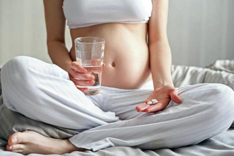 stockphotocloseupofonepregnantwomanwithpillsandglassofwatersittingonthebed1344255191.jpg