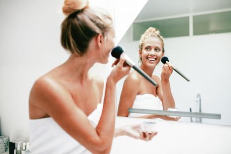 stockphotobeautifulyoungwomanwithbrushapplyingmakeupinbathroomfemalelookingintothebathroom537338236.jpg