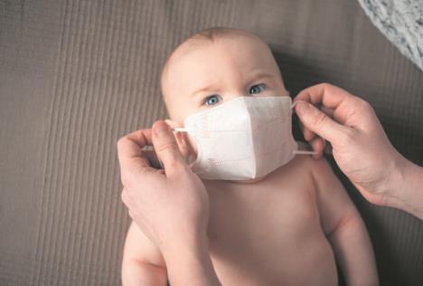 stockphotoparentputsmedicalmaskfromcoronavirusonnewbornbabyonbeddarkbackgroundcloseup1693416058.jpg