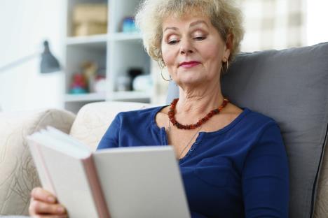 stockphotoportraitofadultwomanreadinginterestingbookagedcurlyhairedgrandmothersittingonsofaat1621474270.jpg