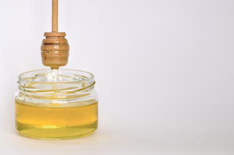 stockphotoglassjarwithhoneyandawoodenstickonawhitebackgroundpouringaromatichoneyintojar1655874790.jpg