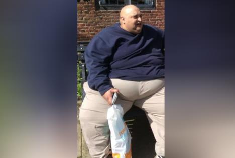 Harvi Olik sedi na klupi sa kesom i telefonom u ruci