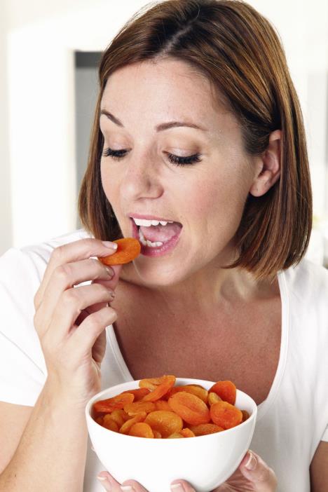 stockphotogirlwithbrownhairwearingawhitetshirtstyletopeatingfromabowlfullofdriedapricot677128321.jpg