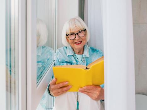 stockphotosenioroldwomanwithgrayhairreadingabookbythewindowathomeeducationpensionanti1776527168.jpg