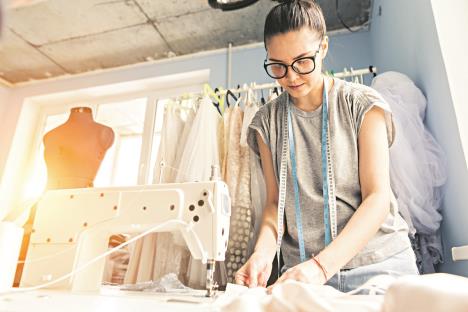 0904-stockphotoyoungdressmakerwomansewsclothesonsewingmachinesmilingseamstressandherhandcloseupin621832295.jpg