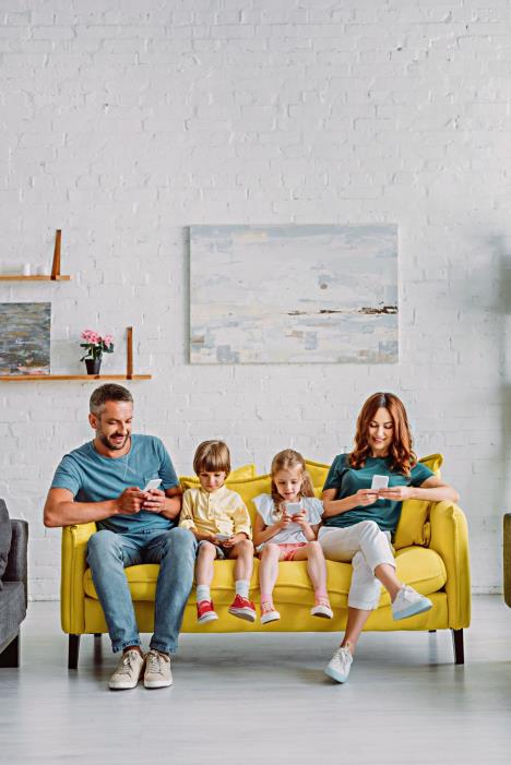 stockphotosmilingfamilyusingsmartphoneswhilesittingonyellowsofaathome1491876080.jpg