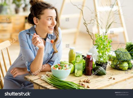 stockphotoyoungandhappywomaneatinghealthysaladsittingonthetablewithgreenfreshingredientsindoors622381814.jpg