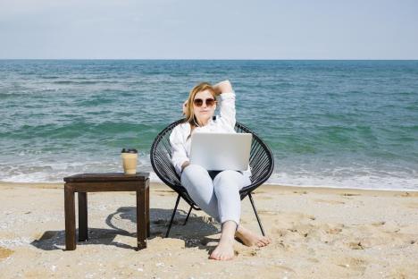 frontviewwomanwithlaptopworkingbeachwithcupcoffee.jpg