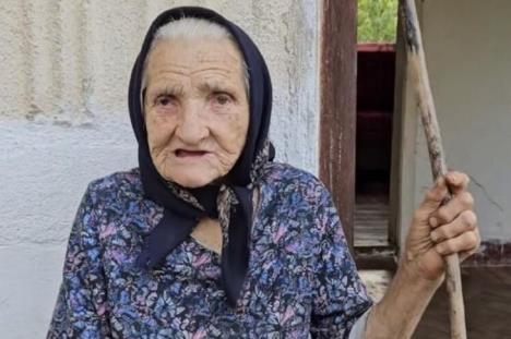 Baka u cvetnoj košulji sa crnom maramom na glavi drži štap u rukama