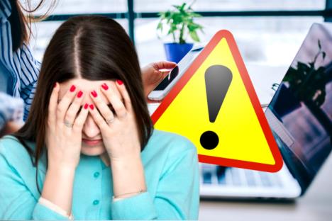 Zabrinuta žena se drži za glavu, u pozadini druga žena drži telefon ispred laptopa, pored znaka upozorenja