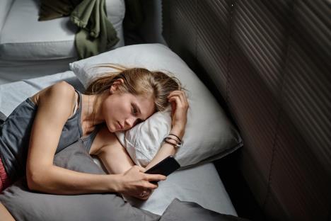 Devojka leži u krevetu i gleda u telefon