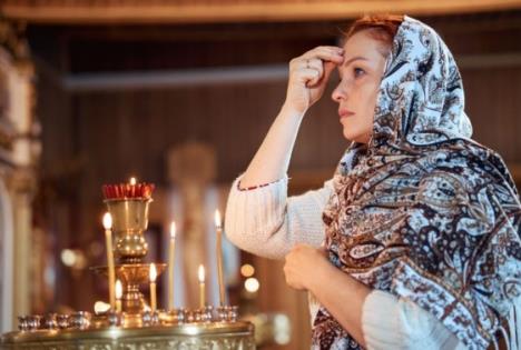 Žena sa maramom na glavi se krsti u crkvi pred upaljenim svećama