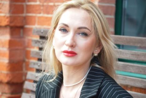 Žena u 40im, plavuša sedi na klupi ispred zgrade