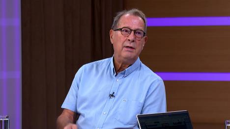 Čovek sa naočarima u plavoj košulji tokom gostovanja u televizijskom studiju