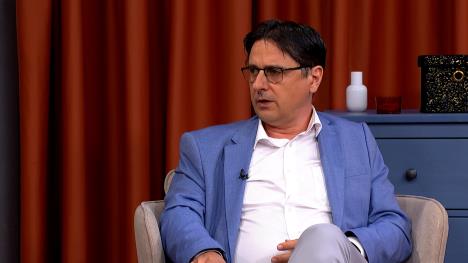 Muškarac sa naočarima, u plavom sakou i beloj košulji u televizijskom studiju.