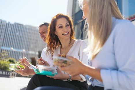 tri osobe sede ispred poslovne zgrade na pauzi za ručak