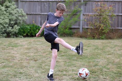 Dečak u šortsu i majici šutira loptu u dvorištu