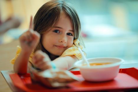 devojčica sedi u školskoj trpezariji sa obrokom ispred sebe i odbija da jede