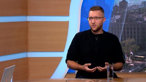 Muškarac sa naočarima, obučen u crno, u televizijskom studiju