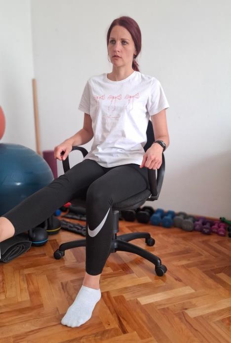 trener sedi na stolici, ruke su položene na rukohvate, levo topalo dodiruje pod, desna noga je podignuta pod uglom od 90 stepeni unapred