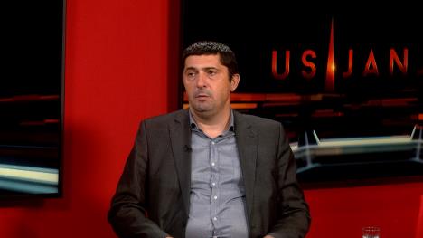 Čovek u sivom sakou, plavoj košulji i crvenoj pozadini