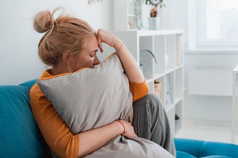žena koja pati sedi na kauču sa zagrljenim jastukom, koncept depresija