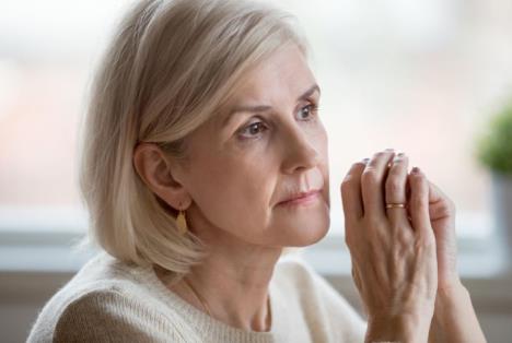 Žena belom džemperu zamišljeno gleda u daljinu