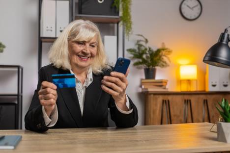 Žena srednjih godina drži telefon i bankovnu karticu u ruci