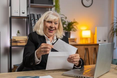 Žena srednjih godina drži papir u ruci i smeje se