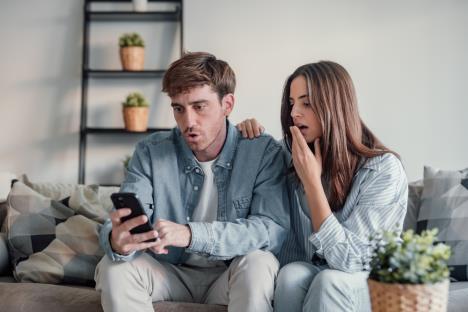 Momak i devojka sede na krevetu i gledaju u mobilni