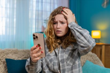 Devojka gleda u mobilni telefon i drži se za glavu