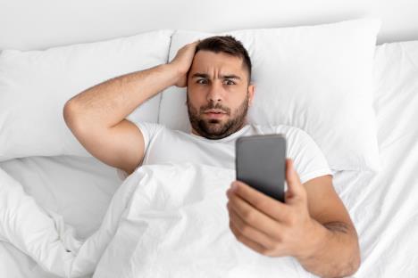 Muškarac gleda u mobilni telefon i leži u krevetu