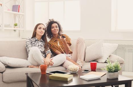 Dve drugarice sede na krevetu i gledaju tv