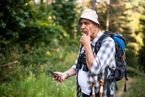 Zamišljen muškarac u šumi drži mobilni telefon