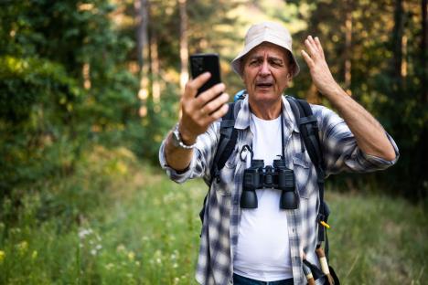 Iznervirani muškarac u šumi gleda u mobilni telefon