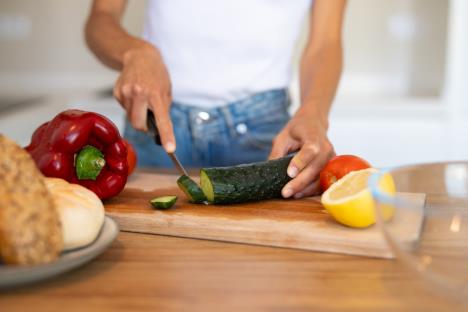 krupan plan devojke u farmerkama i beloj majci koja seče krastavac na drvenoj dasci