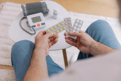 čovek gleda različite lekove dok ispred njega stoji merač za pritisak