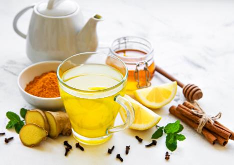 na beloj površini se nalazi iseckan đumbir, šolja napitka žute boje, limun, cimet i čajnik