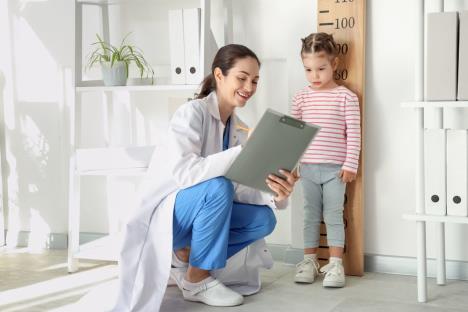 Devojcica kod pedijatra u ordinaciji koja meri njenu visinu i upisuje u zdravstveni karton