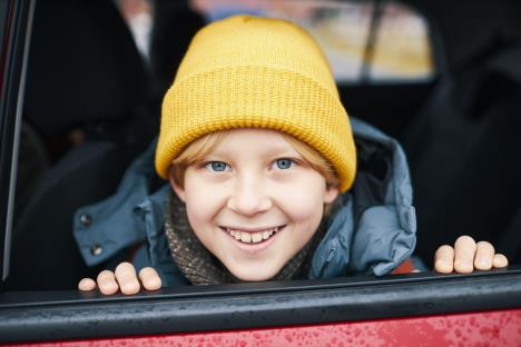 Dečak sa žutom kapom u zimskoj jakni sedi u crvenim kolima