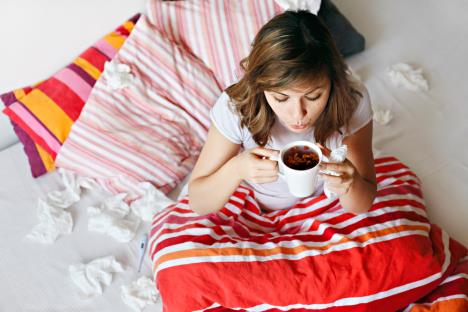 mlada žena sa prehladom sedi u krevetu i pije čaj