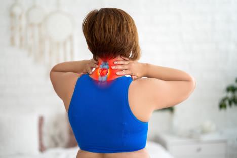 žena u plavom bodiju okrenuta leđima se drži za bolni vrat