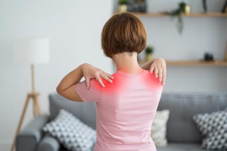 žena u roze majici okrenuta leđima se drži za bolna ramena