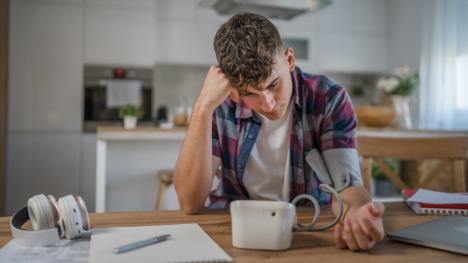 tinejdžer sedi za stolom zabrinut i meri krvni pritisak na levoj ruci