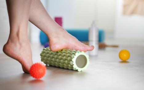 žena masira stopala zelenim rolerom, loptice za masažu pored na podu