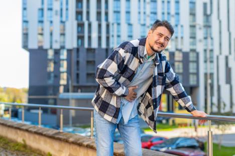 Mlad čovek ima stomačne probleme na putovanju - drži se za stomak