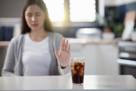 devojka rukom pokazuje negodovanje čaše gaziranog pića na stolu