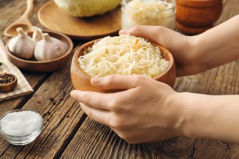 ruke žene drže drvenu činiju sa kupusom ribancem, na stolu so, biber, beli luk, glavica kiselog kupusa
