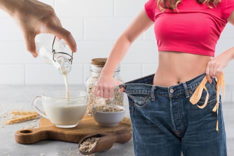 mlada žena koja na farmerkama pokazuje koliko je smršala/ovseno mleko