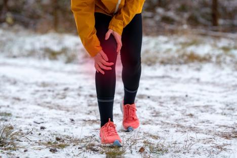 devojka u crnim helankama, žutoj jakni i crvenim patikama drži se za desno koleno